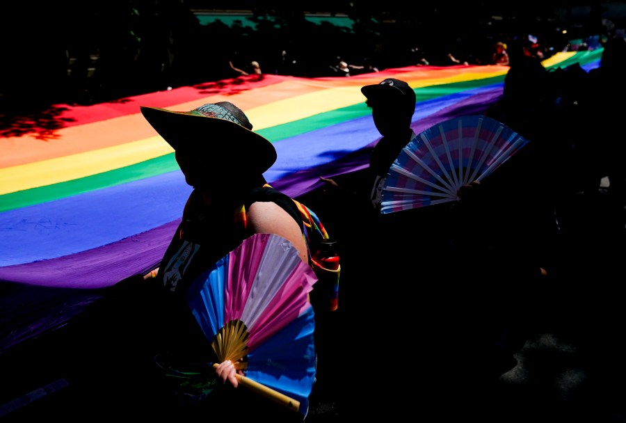 FILE - Mac Weatherill, left, and Yexara Colón Martinez, second from left, hold transgender pride fans as they help carry a large rainbow flag on their fourth anniversary during the annual Seattle Pride Parade, June 25, 2023, in Seattle. (AP Photo/Lindsey Wasson, file)