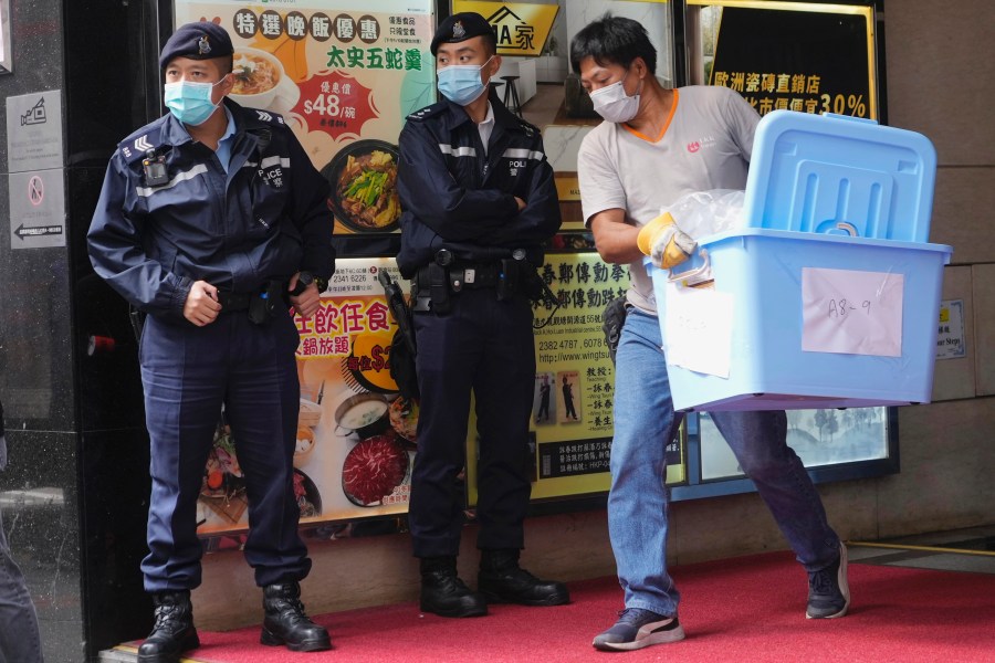 FILE - A worker carrying some containers walks past police officers during a raid on the office of Stand News during a raid in Hong Kong, Dec. 29, 2021. (AP Photo/Vincent Yu, File)