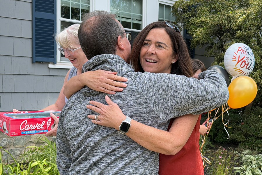 Lori Talanian, right, director of corporate partnerships at Ira Cars, hugs John Quill, center, director and coach of the Boston Bear Cubs hockey team, Wednesday, Aug. 21, 2024, after her company presented the team with a donation of $3,900, at the Doherty family home, in Norwood, Mass. (AP Photo/Rodrique Ngowi)